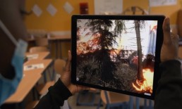 Blick über die Schulter einer Schülerin auf ein Tablett, auf dem die Animation eines Waldbrands zu sehen ist.