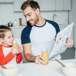Vater und Sohn im Kindergartenalter sitzen am Küchentisch und schen gemeinsam in die Zeitung.