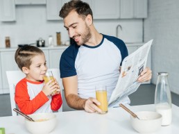 Vater und Sohn im Kindergartenalter sitzen am Küchentisch und schen gemeinsam in die Zeitung.