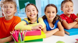 Vier Grundschulkinder sitzen an einem Tisch und lächeln in die Kamera