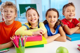 Vier Grundschulkinder sitzen an einem Tisch und lächeln in die Kamera