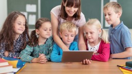 Fünf Grundschulkinder und eine Lehrerin schauen gemeinsam auf ein Tablet.
