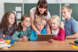 Fünf Grundschulkinder und eine Lehrerin schauen gemeinsam auf ein Tablet.