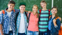 Fünf Jugendliche stehen Arm in Arm vor einer Tafel und lächeln in die Kamera
