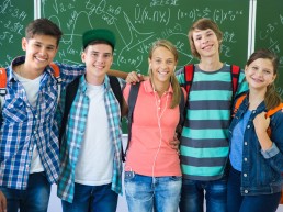Fünf Jugendliche stehen Arm in Arm vor einer Tafel und lächeln in die Kamera